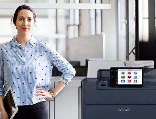 Eine Frau steht neben dem Xerox® PrimeLink® C9200 Serie Drucker in einer modernen Büroumgebung